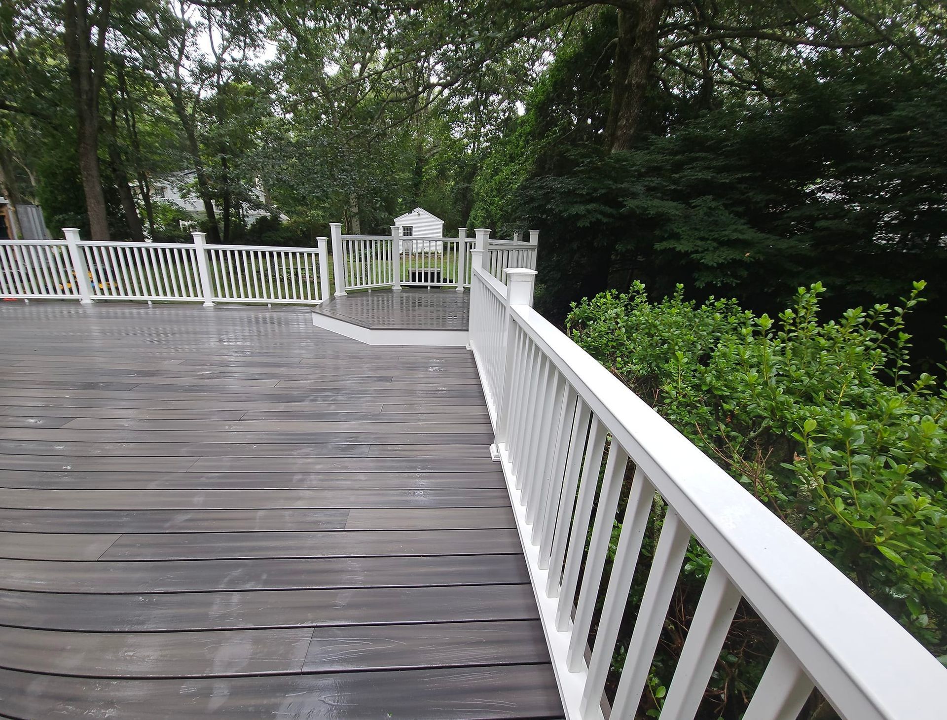 Wooden deck with white railing overlooks green foliage and trees.