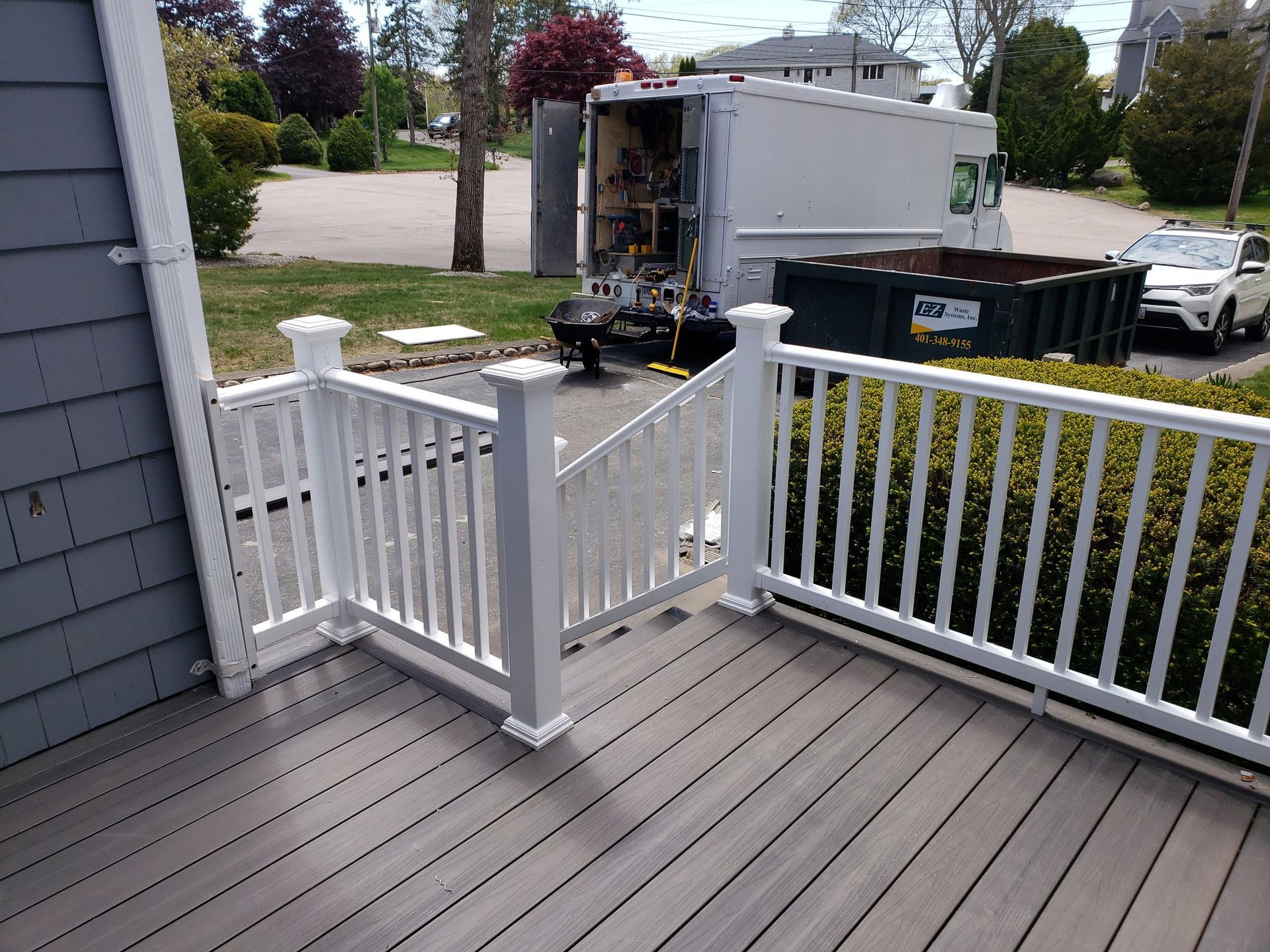 White railing on a composite deck; a truck and dumpster sit in the driveway.