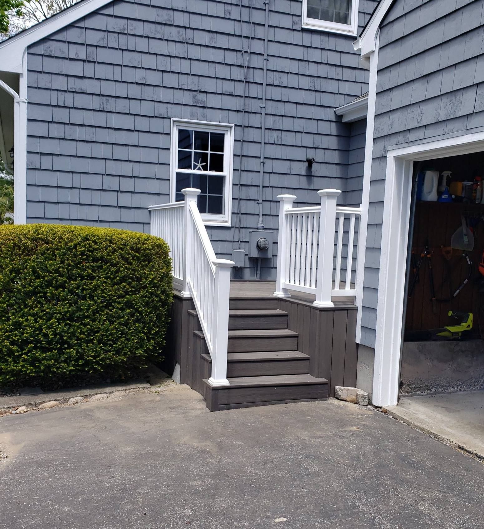 Gray house exterior with a wooden deck and steps leading up to the door, next to a garage.