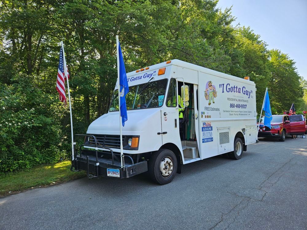 White ice cream truck with flags parked on a road, trees in the background.