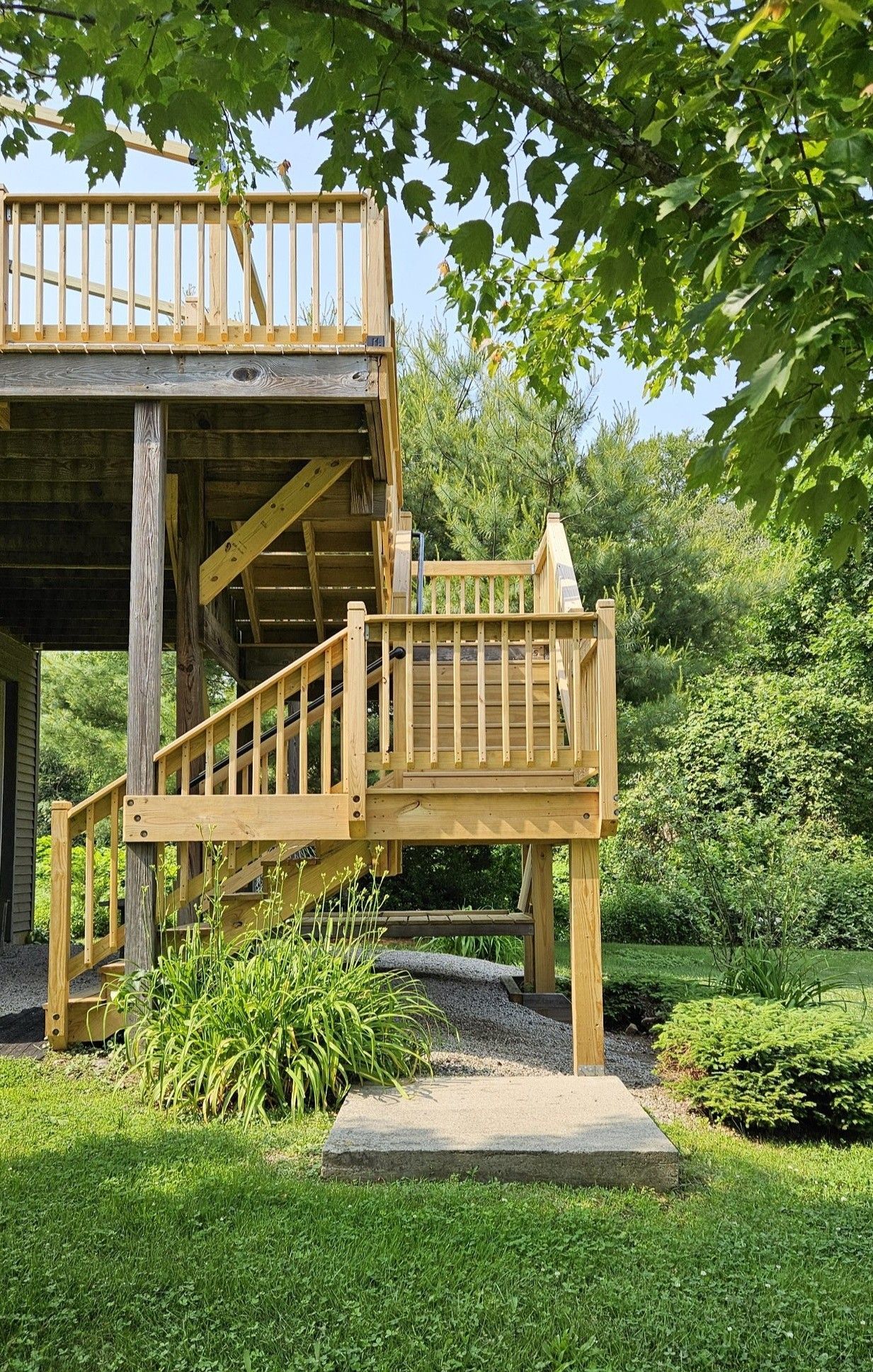 Wooden multi-level deck with stairs in a grassy yard, surrounded by trees.