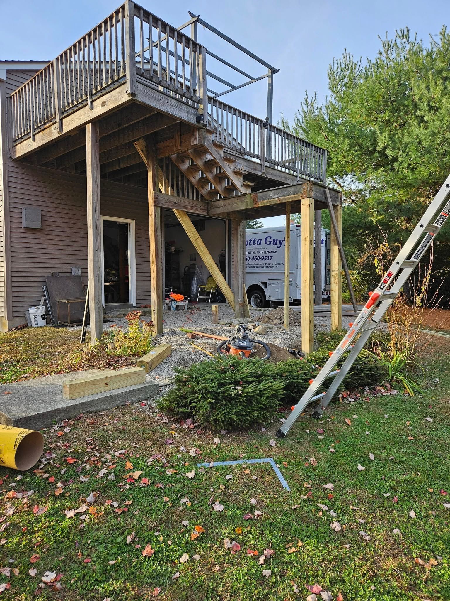 A wooden deck with a staircase under construction; a ladder leans against it.