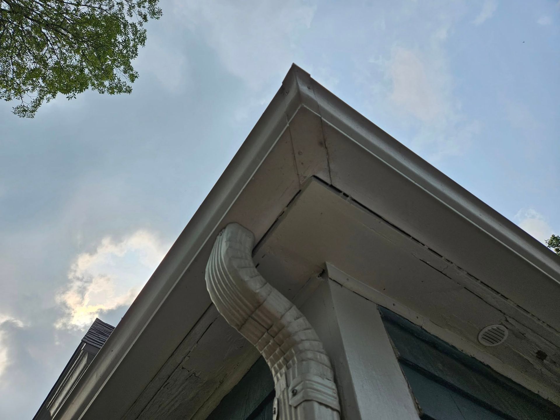 Corner of a white house with gutters, downspout, and cloudy sky visible.