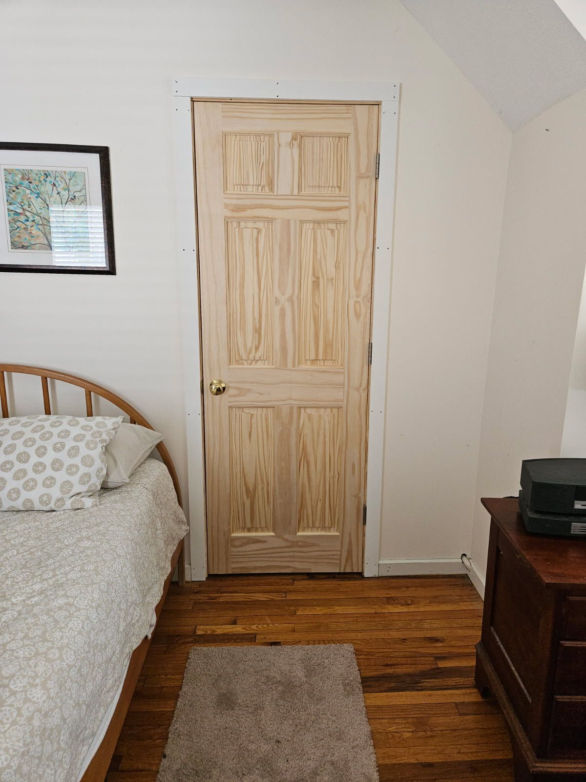 A bedroom with a wooden door, bed, rug, and dresser. The door is centered.