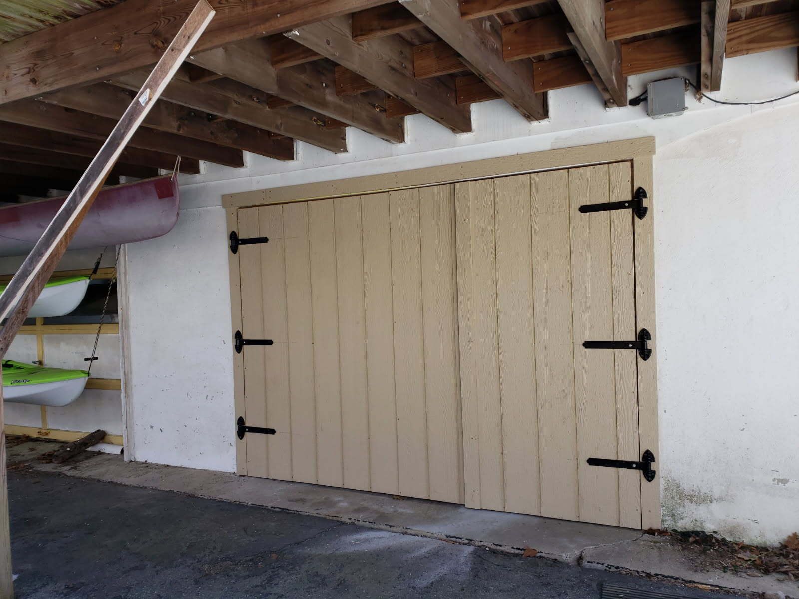 Wooden double doors with black hinges, under a boathouse roof, kayaks visible to the left.
