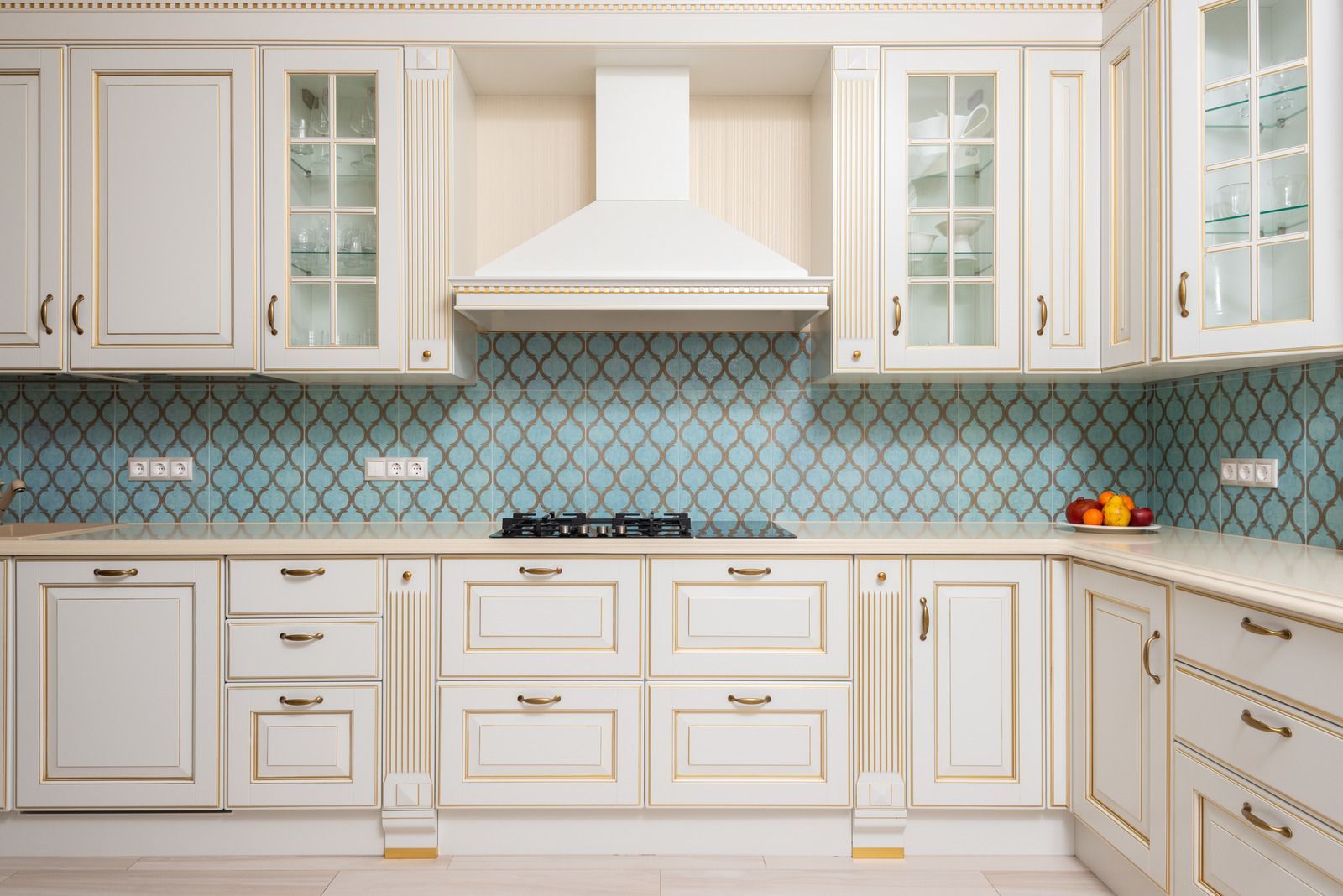 Cream-colored kitchen cabinets with gold trim, blue tile backsplash, and range hood.