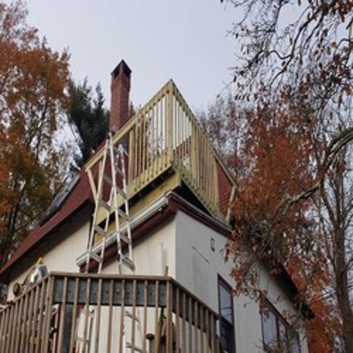 A house with a newly constructed rooftop deck and a ladder leading to it, surrounded by trees.