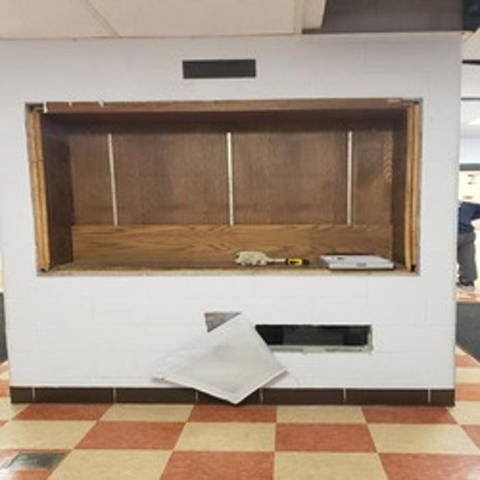 Empty recessed wall niche with a lower rectangular opening. Inside is unfinished wood and tools. White wall, tile floor.