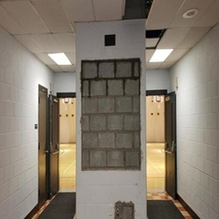Hallway with a column displaying exposed cinder blocks; doors on either side, lights in the ceiling.