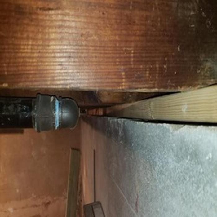Black pipe near a wood beam, next to a gray concrete wall.