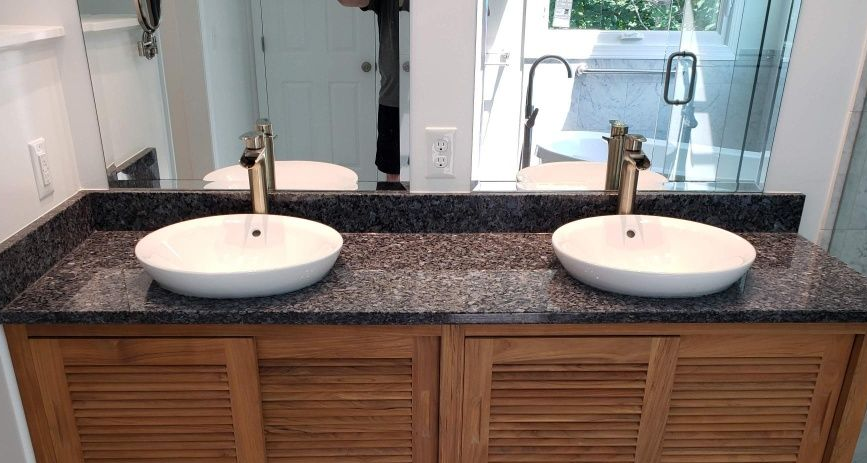 Double vanity with two round sinks, dark granite countertop, and mirrors in a bright bathroom