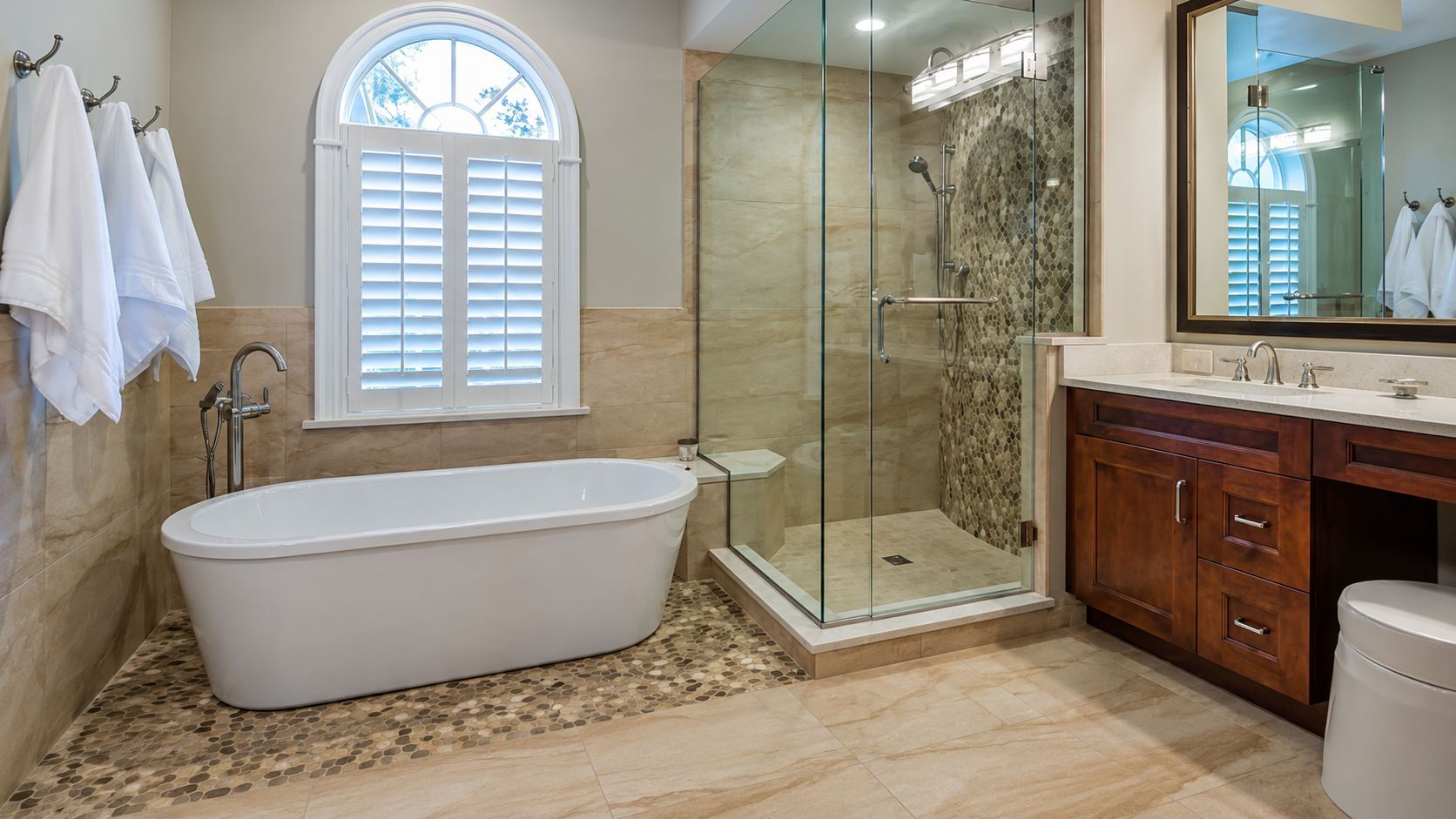 Luxurious bathroom with freestanding tub, glass shower, double vanity, and arched window