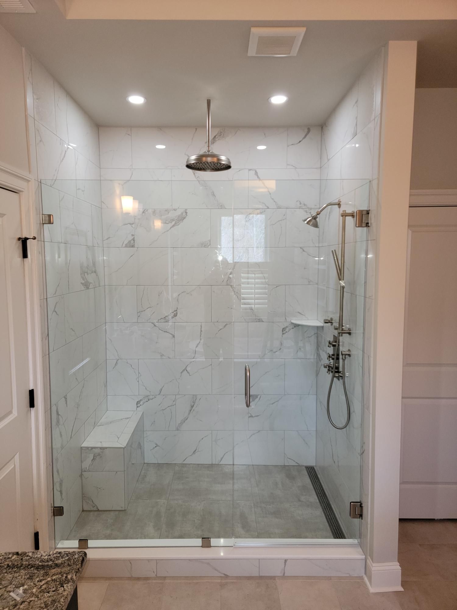 Modern glass walk-in shower with marble tile, rainfall showerhead, and handheld sprayer