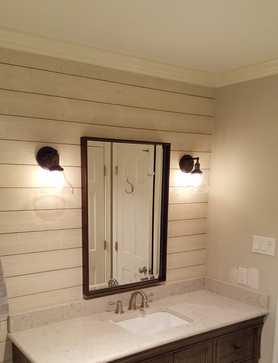 Bathroom vanity with white sink, mirror, and wall sconces against beige striped walls.