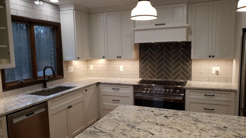 Modern kitchen with white cabinets, granite countertops, pendant light, and herringbone tile backsplash