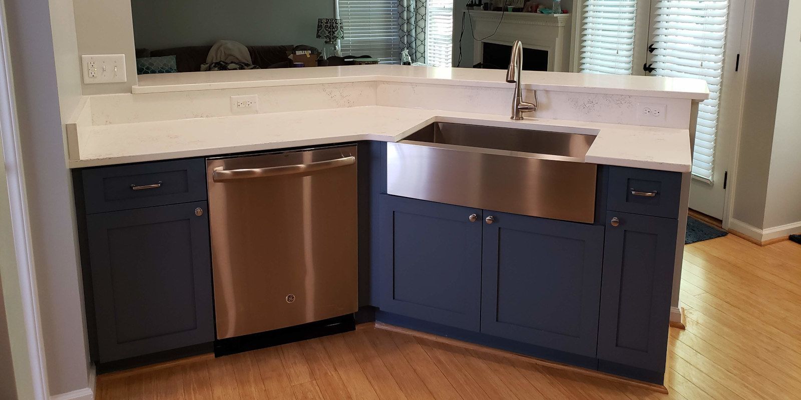 Modern kitchen island with dark blue cabinets, copper dishwasher, and stainless sink under a mirror backsplash
