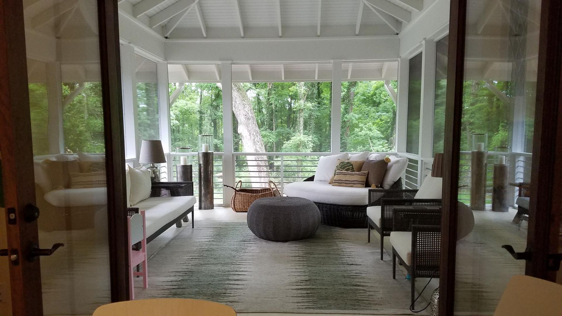 Bright white screened porch with wicker sofa, ottoman, and green views outside