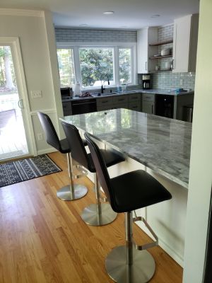 Modern kitchen with marble island, three bar stools, hardwood floors, and large window.
