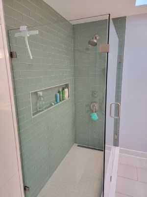Small tiled shower stall with green subway tiles, wall niche, and glass door in a bathroom.