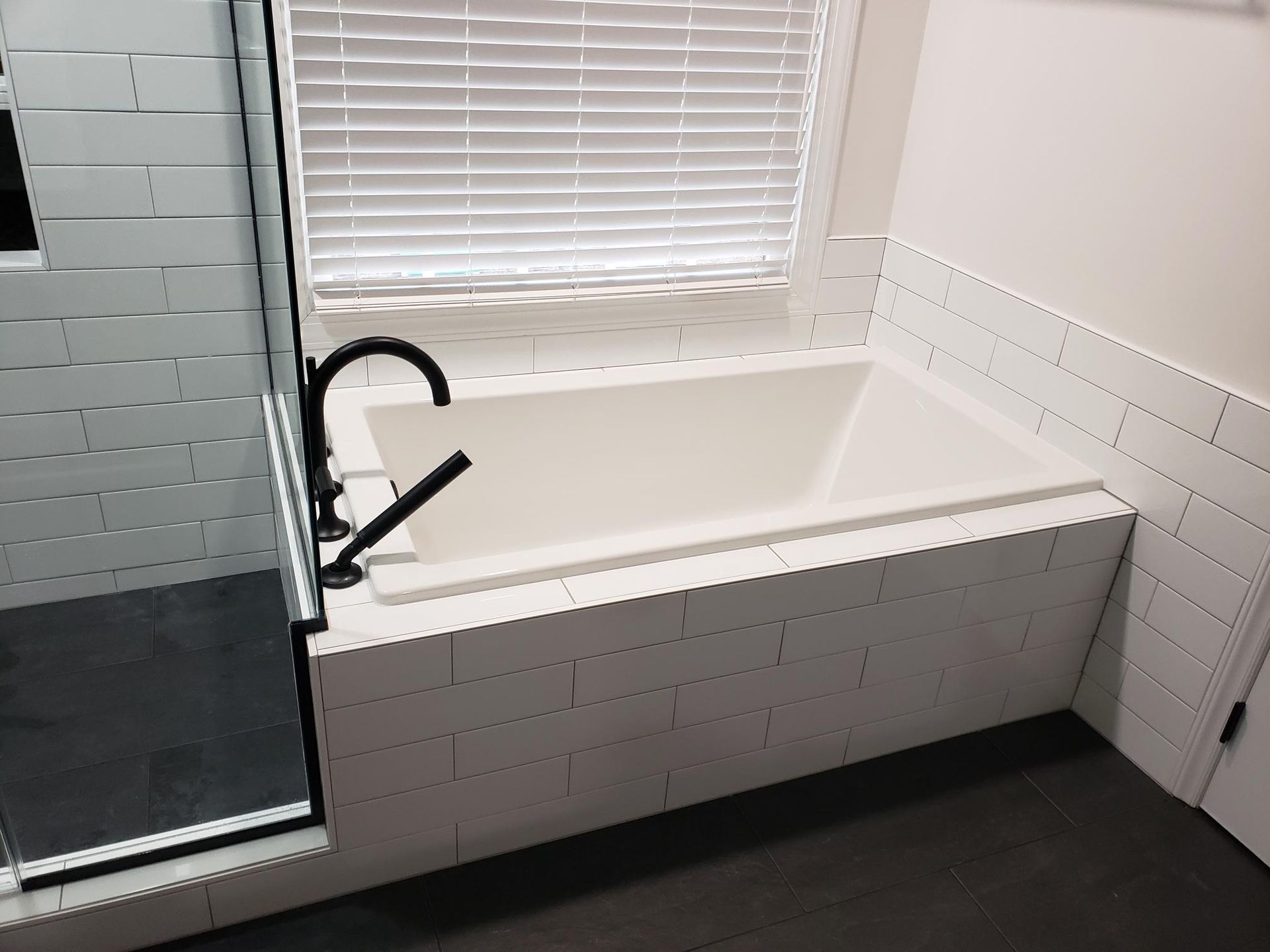 Accessible bathroom with walk-in tub, black faucet, and white tile walls near a window.