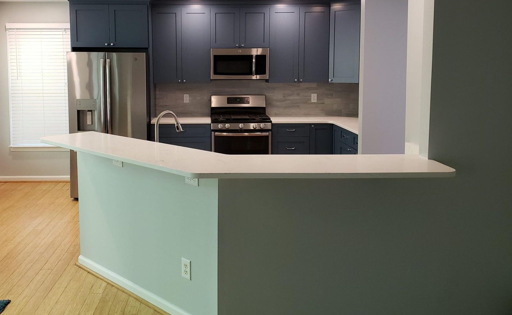 Modern kitchen with blue cabinets, white countertops, stainless appliances, and a mint-green peninsula counter