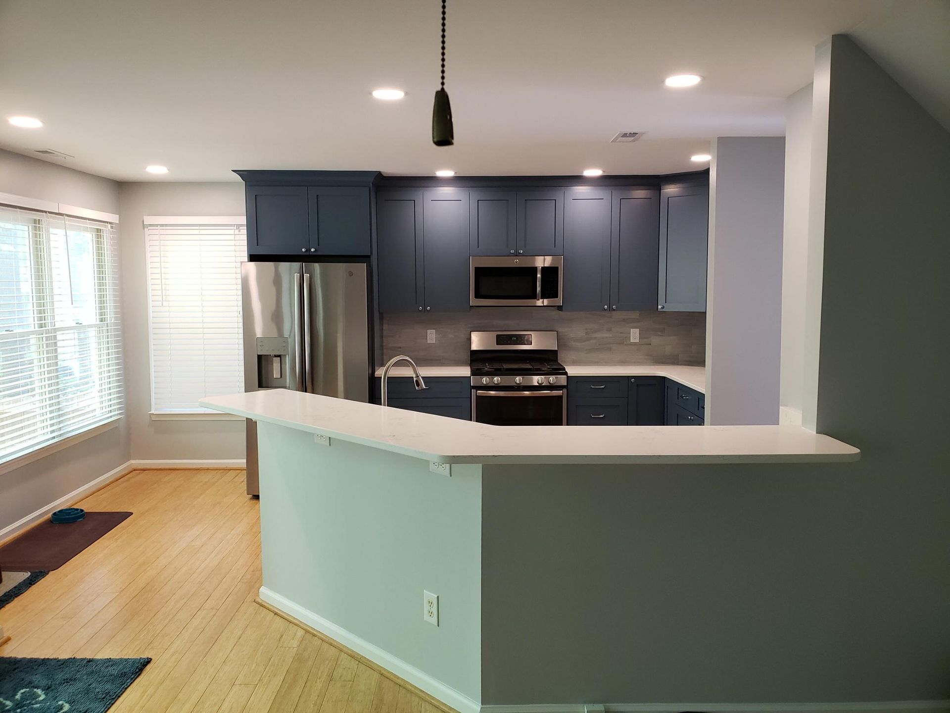 Open-concept kitchen with blue cabinets, stainless appliances, white countertops, and a curved breakfast bar