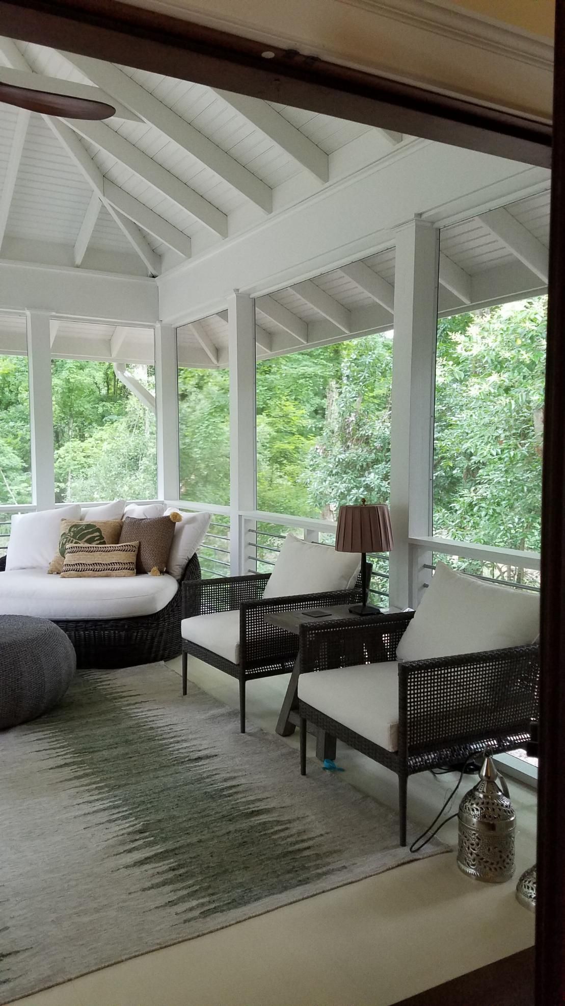 Covered porch with white vaulted ceiling, wicker chairs, sofa, and green forest view