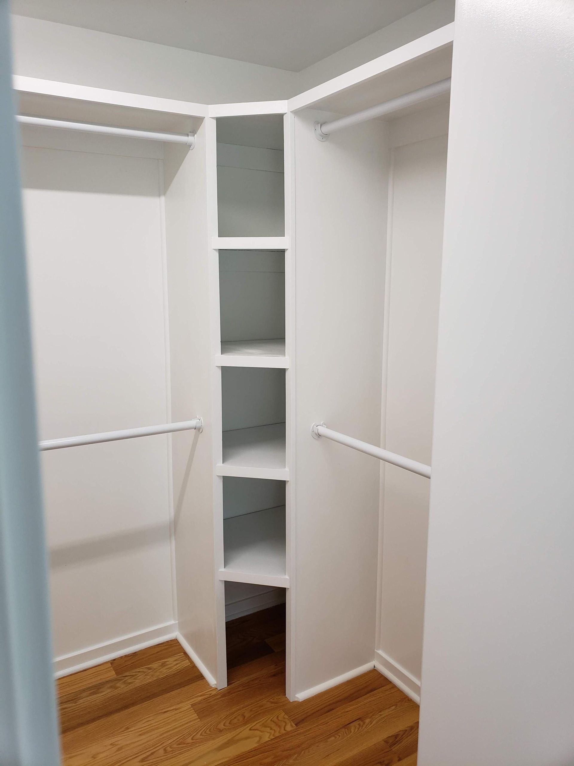Empty walk-in closet with white shelves, hanging rods, and a hardwood floor.