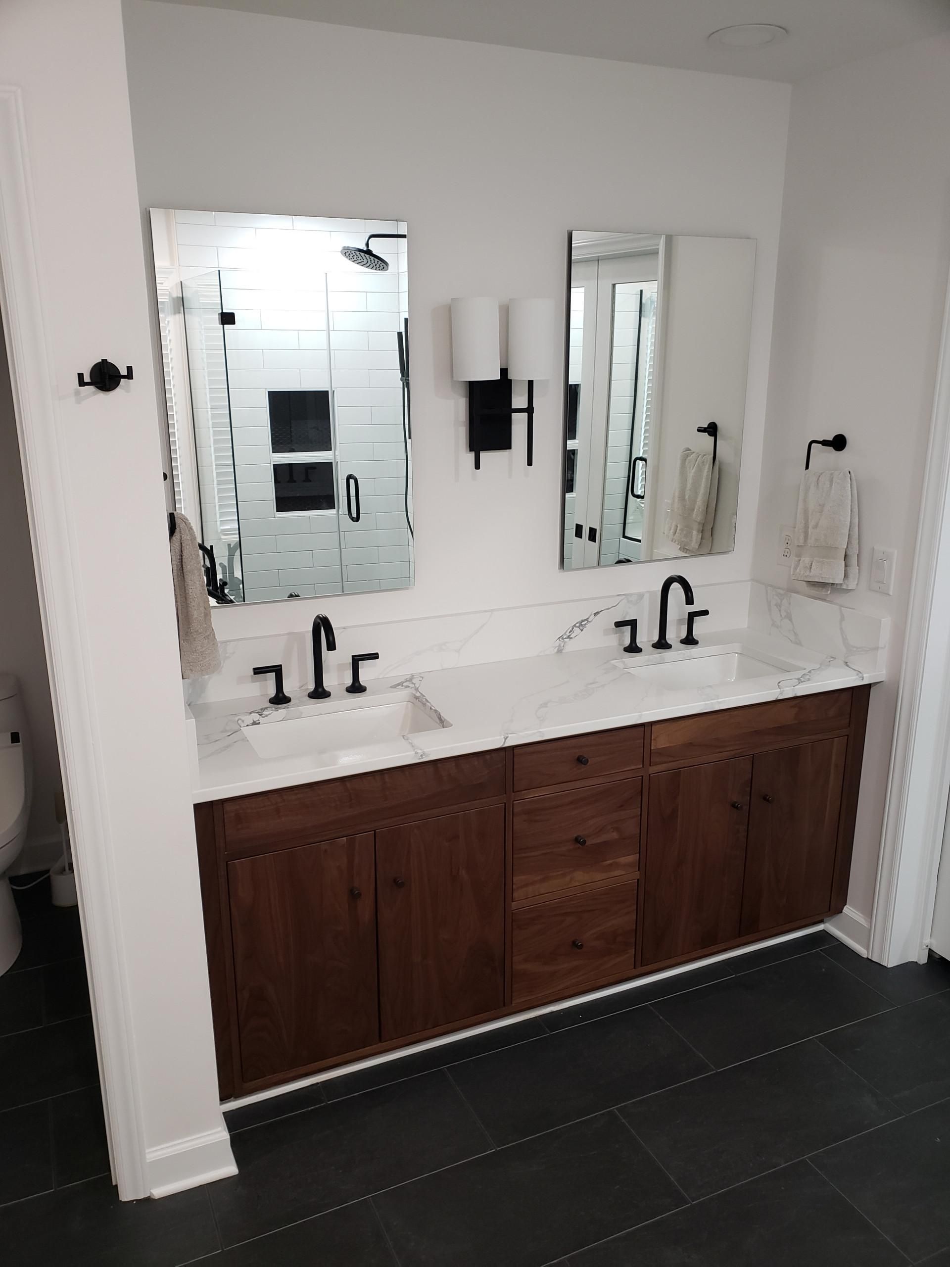 Double vanity bathroom with dark wood cabinets, two mirrors, and white countertop sinks on a dark tile floor