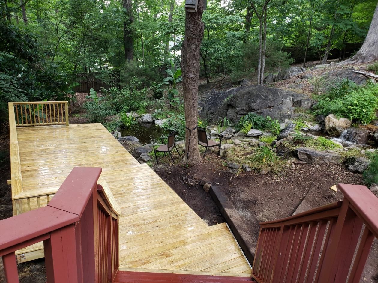 Wooden boardwalk with red railings leading into a green forest by a small rocky stream