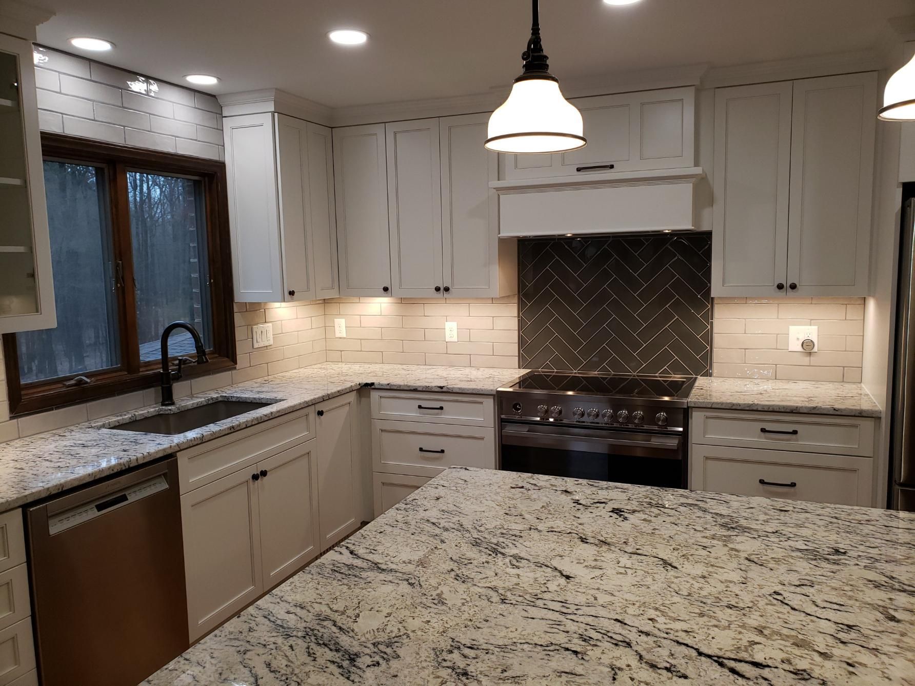 Modern kitchen with white cabinets, granite countertops, stainless appliances, and a pendant light over an island.