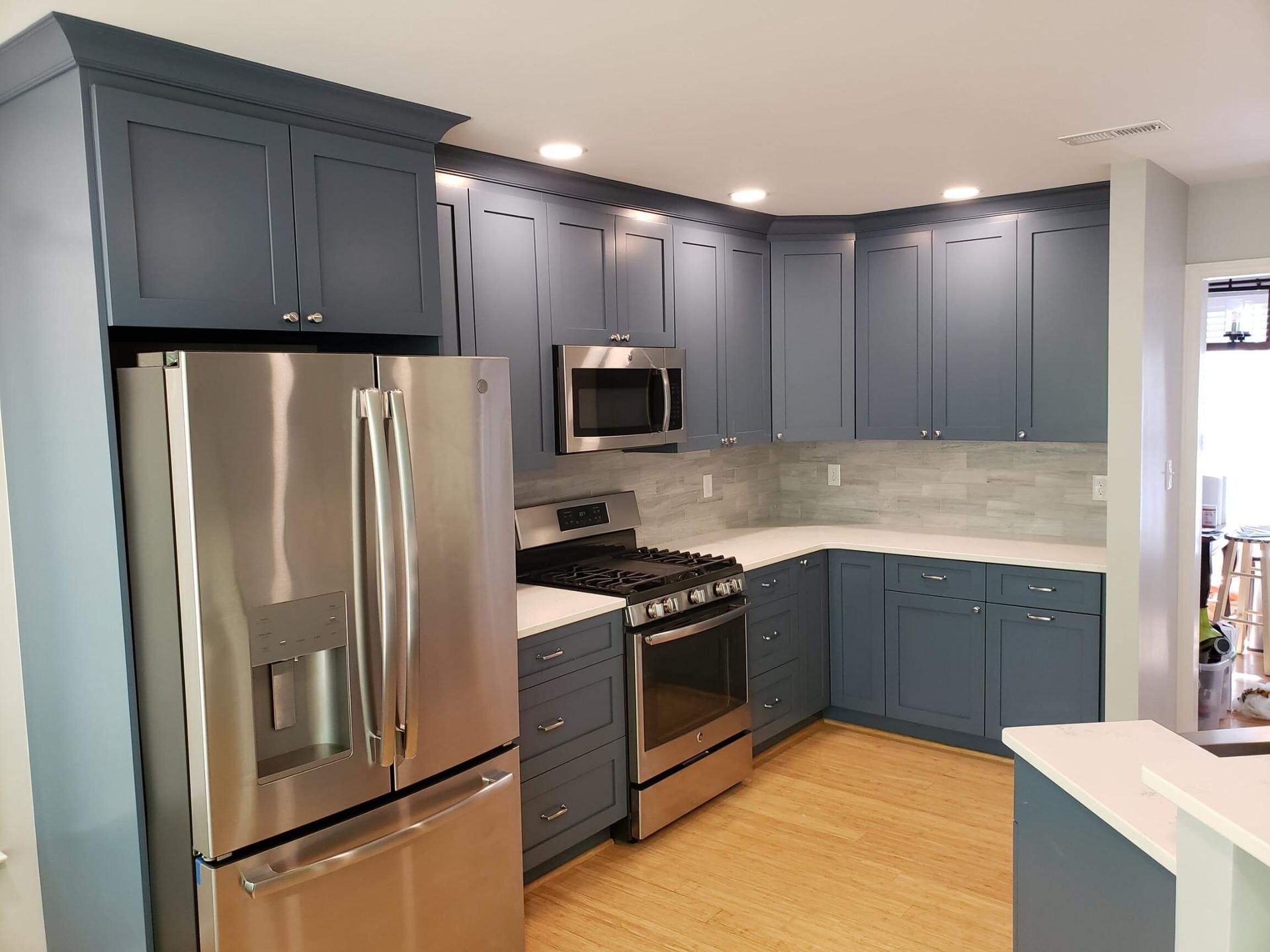 Modern kitchen with blue-gray cabinets, stainless steel appliances, and light wood flooring