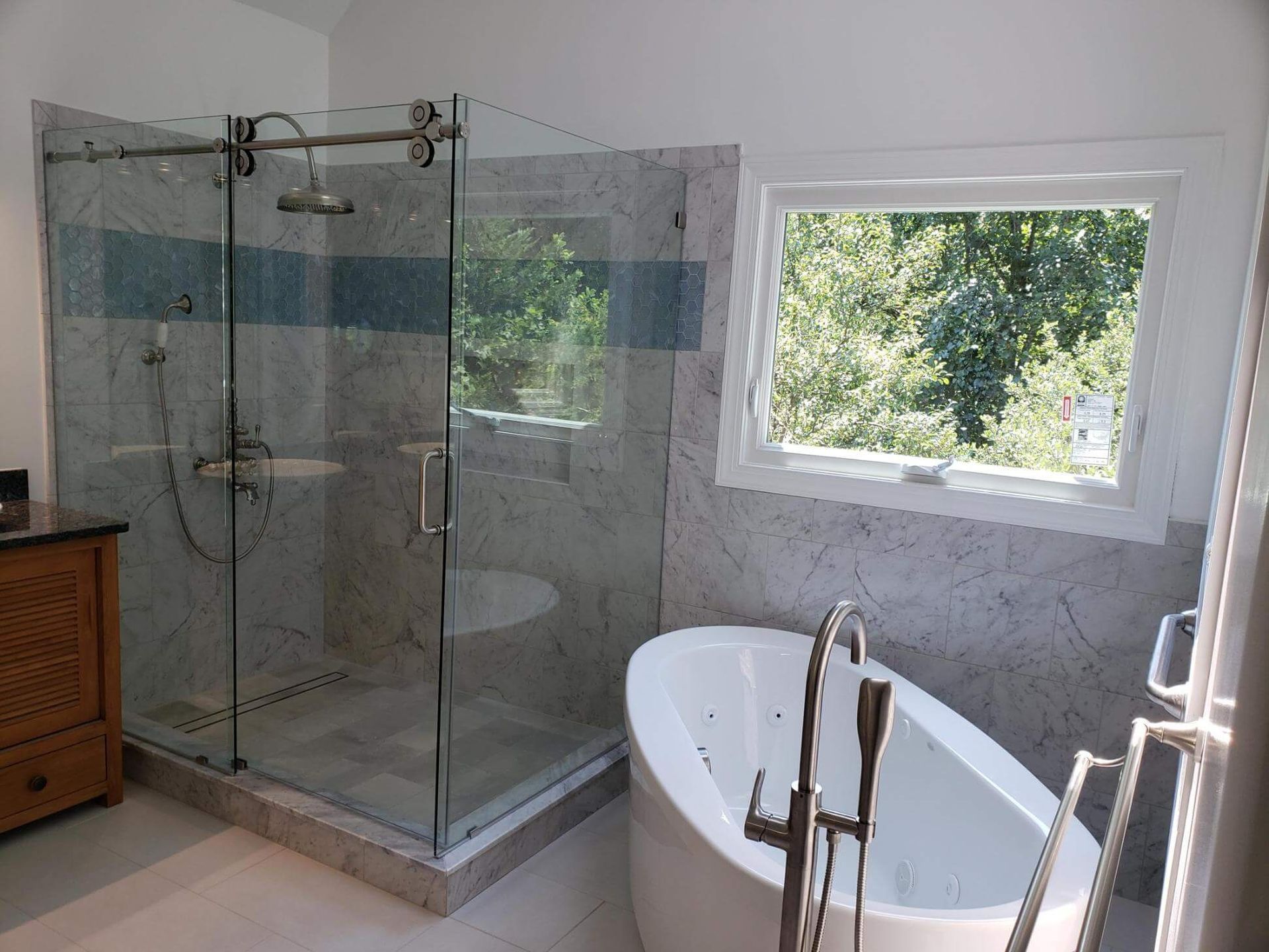Modern bathroom with glass shower, freestanding tub, and large window overlooking greenery