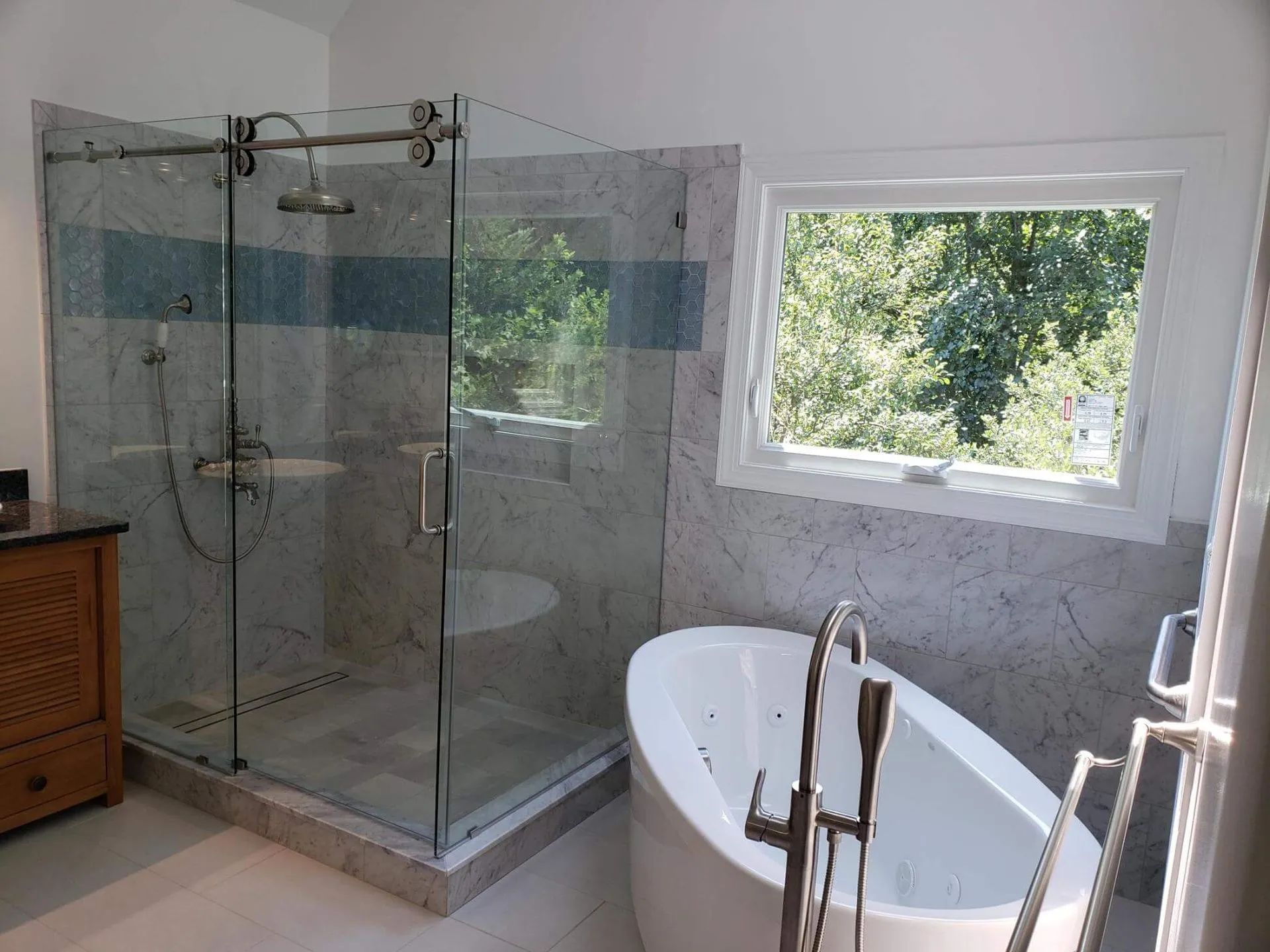 Modern bathroom with glass walk-in shower and white freestanding tub beside a window