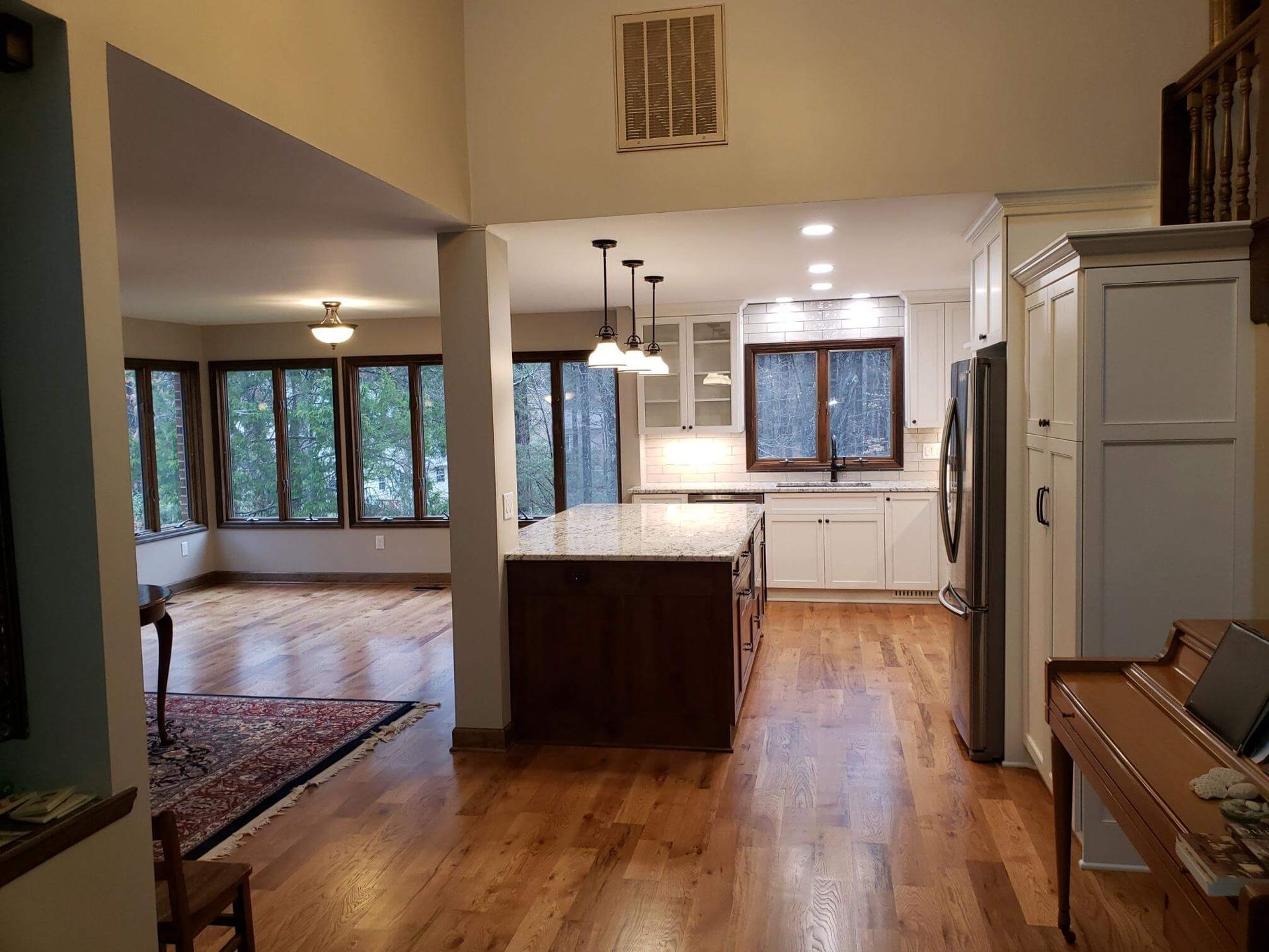 Open kitchen and living room with wood floors, pendant lights, dark island, and large windows.