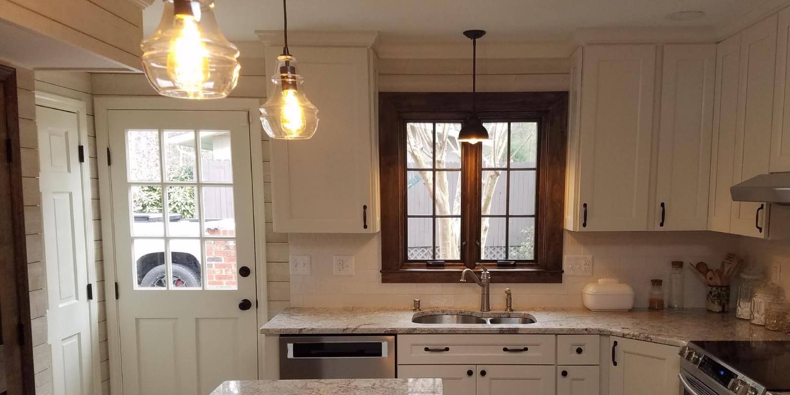 Bright white kitchen with pendant lights, cabinets, stove, and a window over the sink