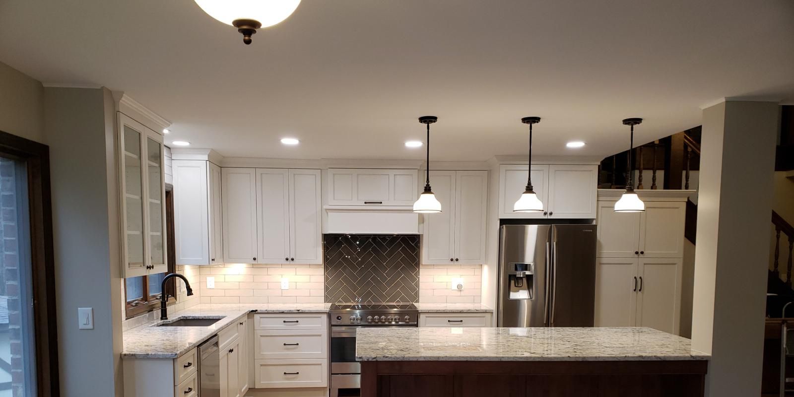Modern white kitchen with island, pendant lights, granite counters, and stainless steel refrigerator