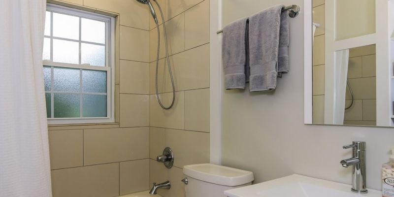 Small bathroom with a bathtub, toilet, window, and towels hanging on the wall.