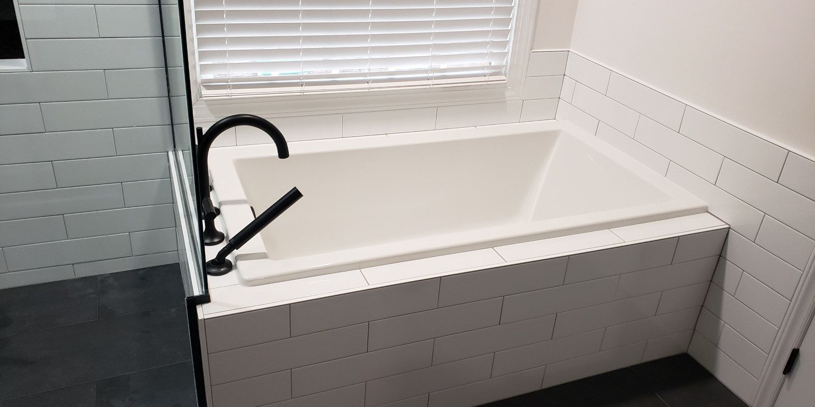 White bathtub with black faucet beside a window in a bright tiled bathroom
