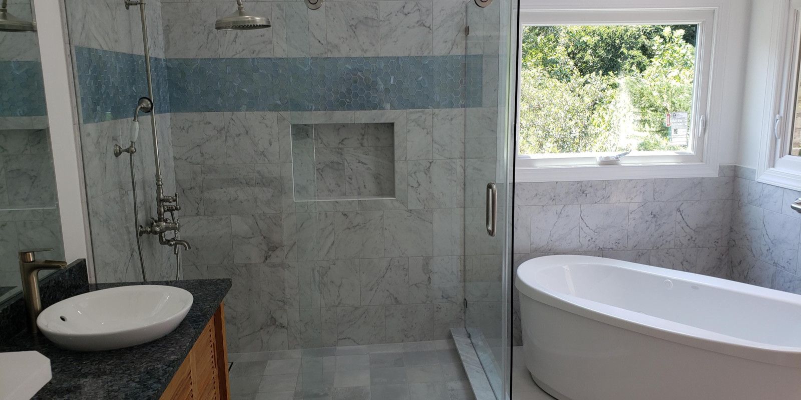 Modern bathroom with glass shower, white vessel sink, and a freestanding bathtub by a window