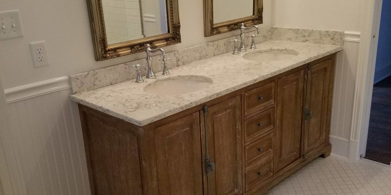 Bathroom vanity with two sinks, marble countertop, and wood cabinets beneath mirrors