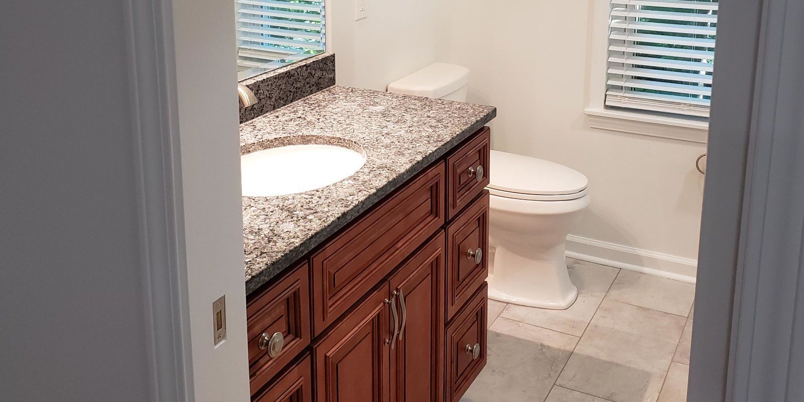 Bathroom with dark wood vanity, granite countertop, and toilet on light tile floor.
