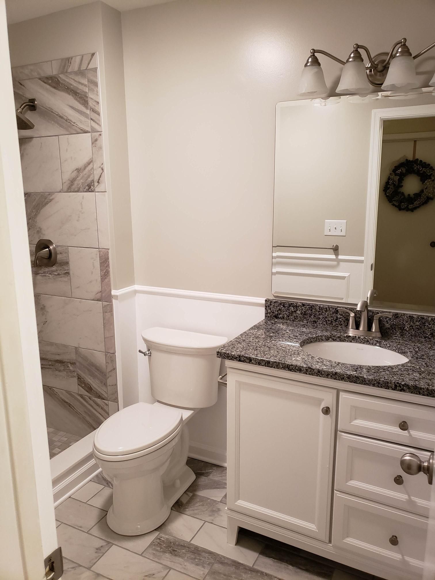 Bathroom with toilet, vanity sink, mirror, and tiled shower in neutral tones.