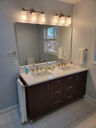 Bathroom vanity with dark cabinets, white sink countertop, mirror, and three-light fixture above.