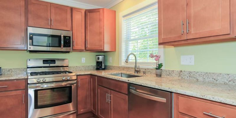 Bright kitchen with wood cabinets, stainless steel appliances, and a granite countertop by a window.