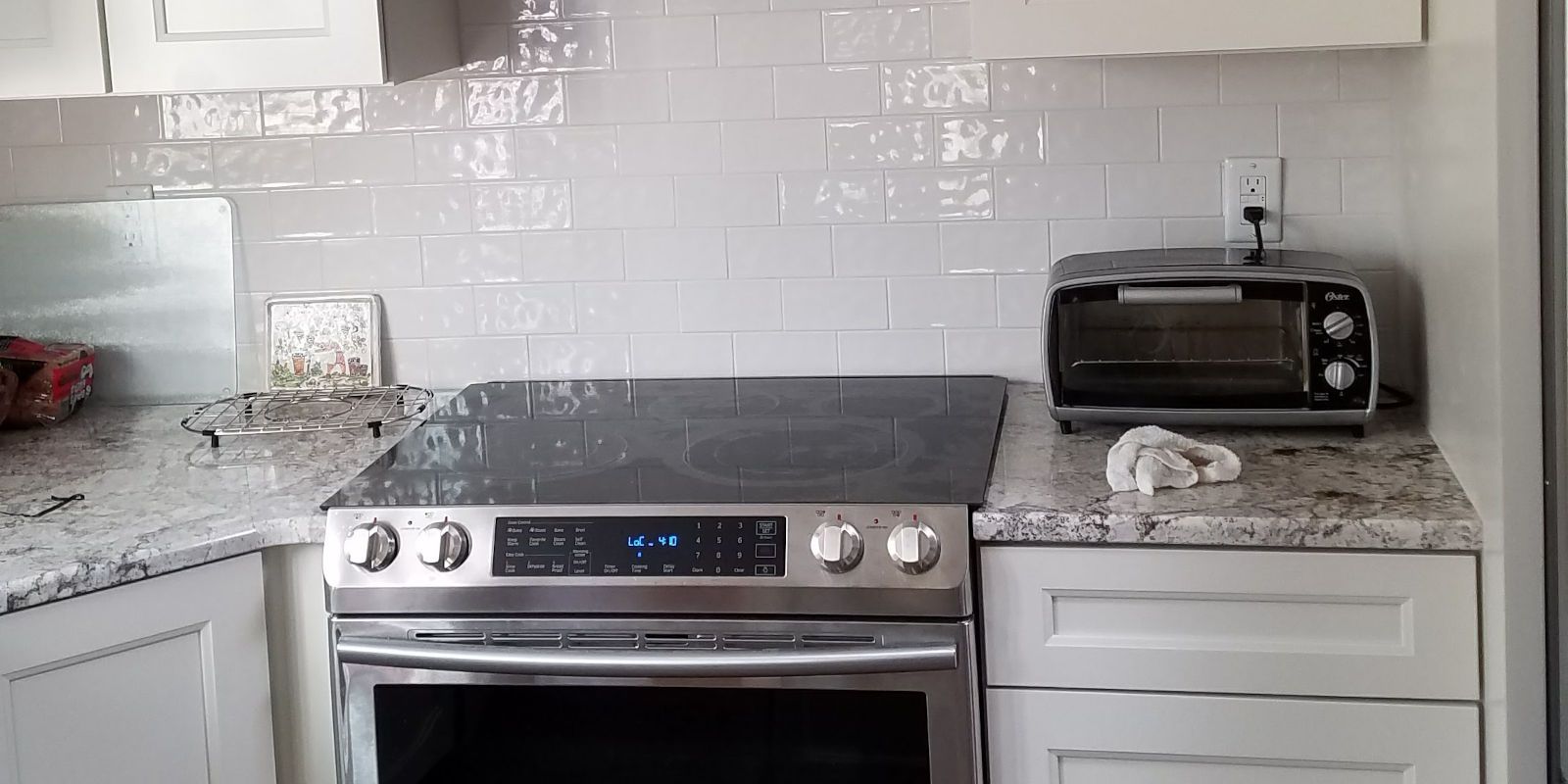 Modern kitchen with a stainless steel stove, white cabinets, granite counters, and a toaster oven.
