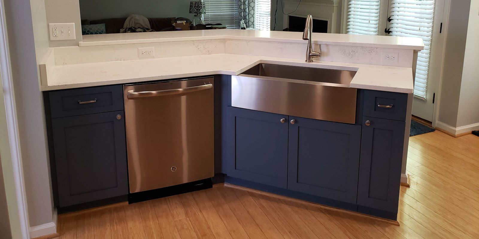 Modern kitchen with dark blue cabinets, copper dishwasher, and stainless farmhouse sink on light countertop