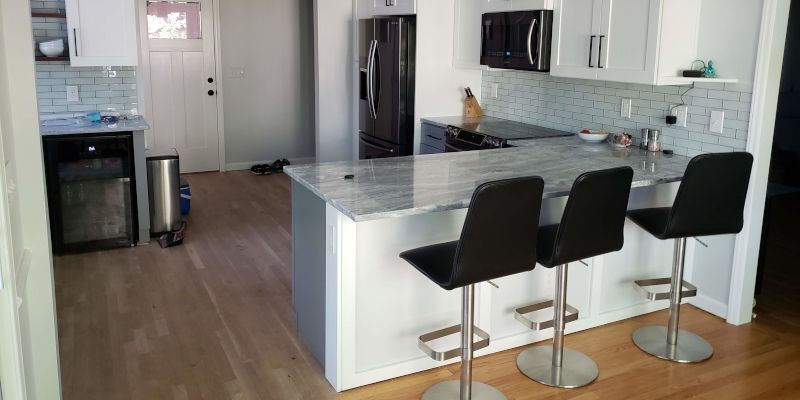 Modern kitchen with white cabinets, gray island, black stools, and stainless steel appliances