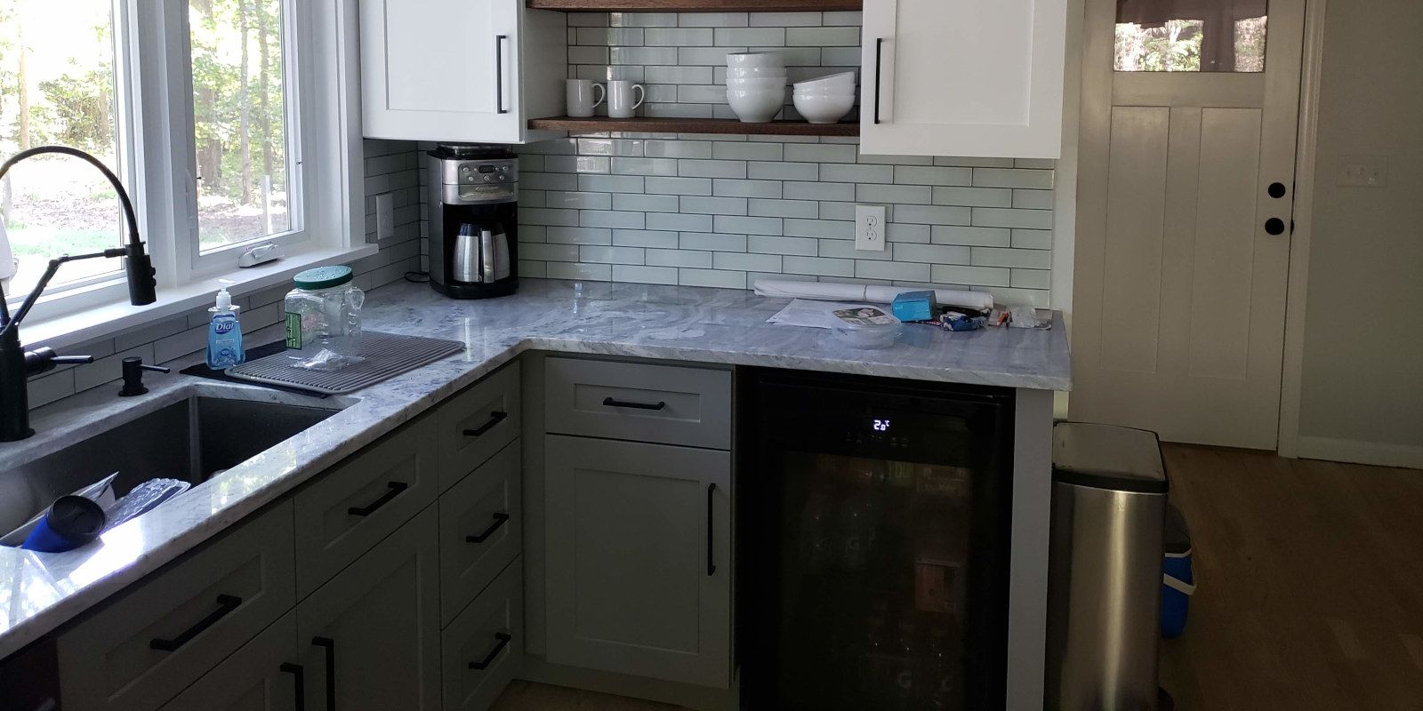 Compact kitchen with gray cabinets, marble-look counters, sink by window, and a small black fridge under the counter
