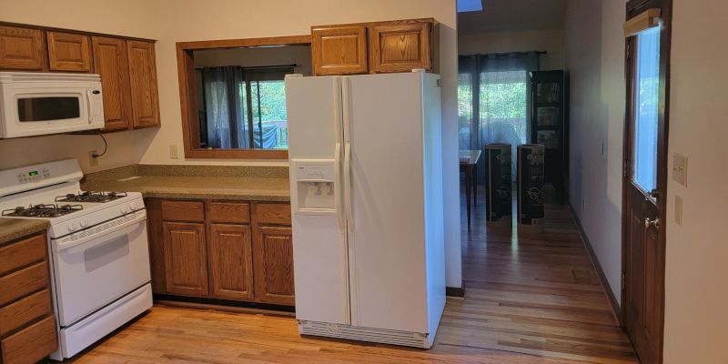 Kitchen with white appliances, wooden cabinets, and a doorway leading to a dining area